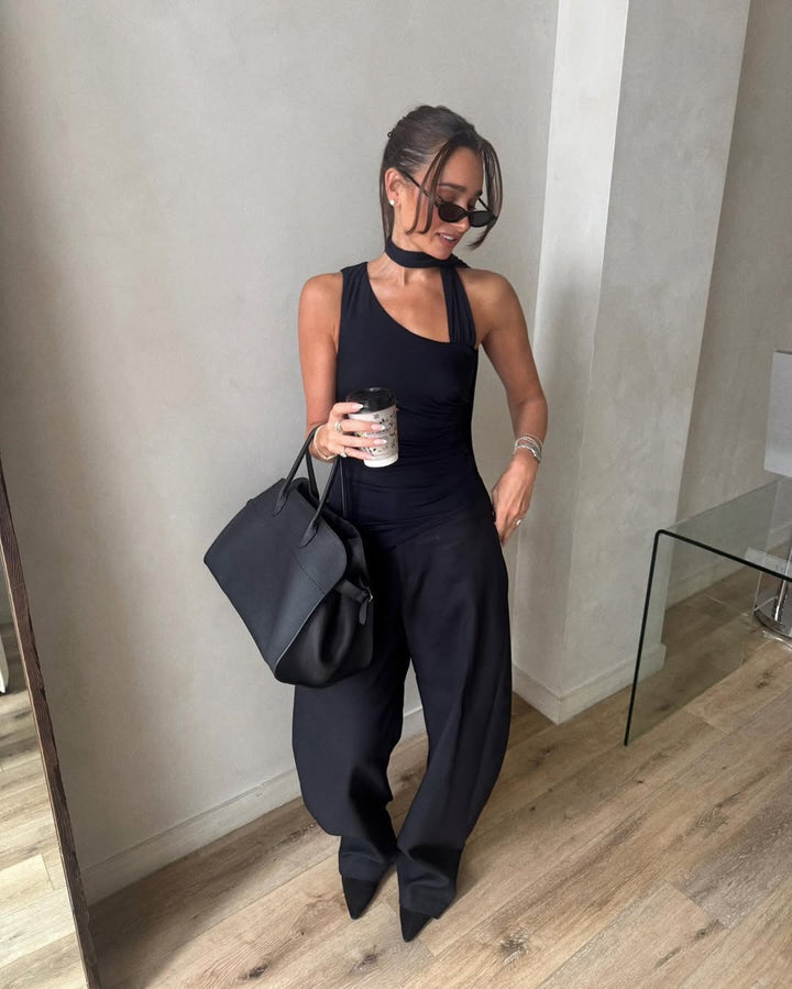 Danielle Bernstein in a navy outfit holding a coffee cup and a black bag indoors.